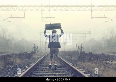 una persona solitaria che si rilassa sulle rotaie in attesa del allenati in una giornata di nebbia Foto Stock