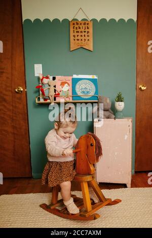 Ragazza del toddler in stanza su cavallo dondolante Foto Stock