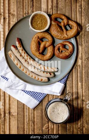 Salsicce di maiale bavaresi alla griglia su piatto di ceramica servite con senape dolce tedesca, tazza di birra scura e pane pretzel su na bianca e blu Foto Stock