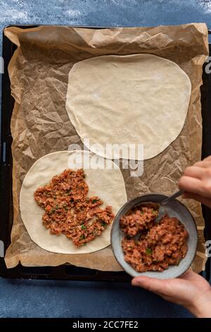 Donna che fa il lahmacun da zero con pasta fatta in casa e ripieno di manzo macinato su una carta pergamena fiancheggiata da forno. Foto Stock