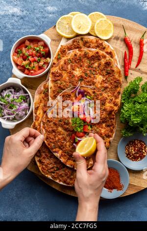 Donna che spreme il limone su un lahmacun servito su una tavola di legno. Più porzioni di lahmacun, insalata di cipolla rossa, insalata di pomodoro, peperoncino in polvere, fiocchi di pepe rosso, Foto Stock