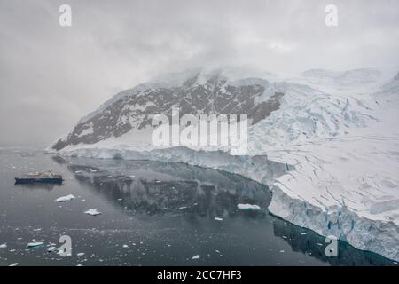 Una nave da crociera Quark Expeditions in una baia circondata da montagne ricoperte di ghiacciaio in Antartide. Foto Stock