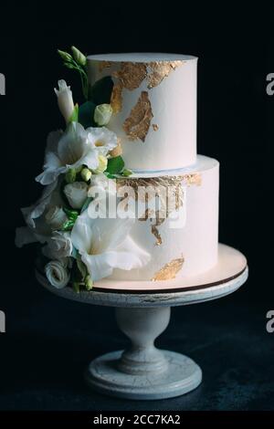 Due livelli di torta con fiori su un supporto di legno su uno sfondo nero. Foto Stock