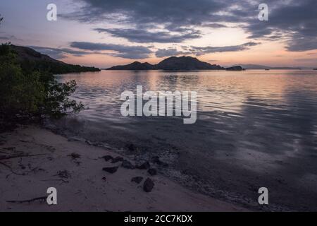 Il cielo si riflette nel mare durante la tarda sera, mentre l'oscurità cade nel Parco Nazionale di Komodo, Indonesia. Foto Stock