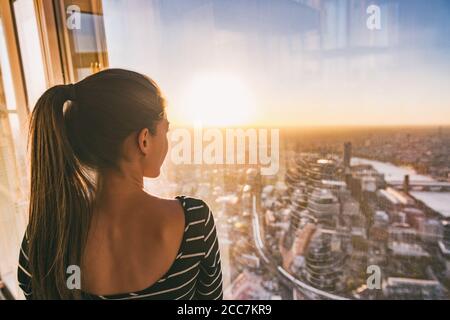 Donna di viaggio in Europa che guarda al tramonto lo skyline della città di Londra dalla finestra dell'alto grattacielo torre, famosa attrazione turistica negli Stati Uniti Foto Stock