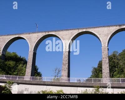 gigantesco e impressionante viadotto ferroviario senza treno di fronte al blu cielo e verde foresta con una strada e guardrail vicino giorno senza persone Foto Stock