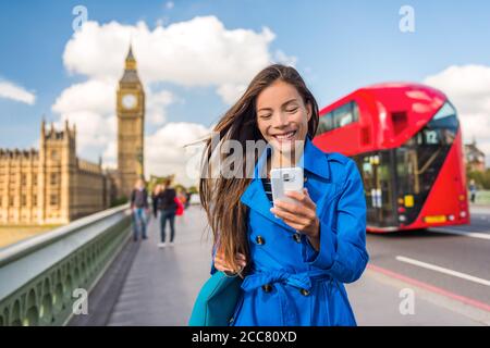 Telefono di Londra donna di affari SMS su smartphone app mobile per il pagamento o lo shopping online. Città urbana stile di vita asiatica ragazza felice camminare sul Big ben Foto Stock