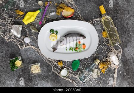 piatto di pesce bianco con trote arcobaleno, piselli, carote, limoni e vari rifiuti nella rete da pesca su un tavolo di marmo grigio Foto Stock