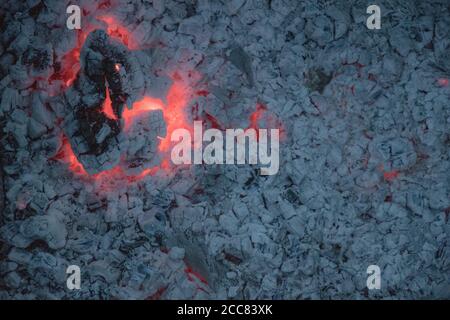 Grande pezzo spaccato di legna da ardere di sbavatura con fiamma rossa all'interno e fondo di cenere grigio. Closeup di tessitura del falò bruciato. Surf di carbone di legno che brucia Foto Stock