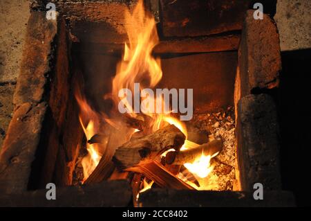 Fiamme sfocate sopra il vecchio mangal in mattoni di terracotta ricoperti di ceneri grigie. Sfondo astratto di Fiery. Foto Stock