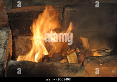 Movimento sfocato di fiamme sopra il vecchio mangal fatto di mattoni di terracotta ricoperti di ceneri grigie. Falò in braciere di carbone con grunge scuro Foto Stock