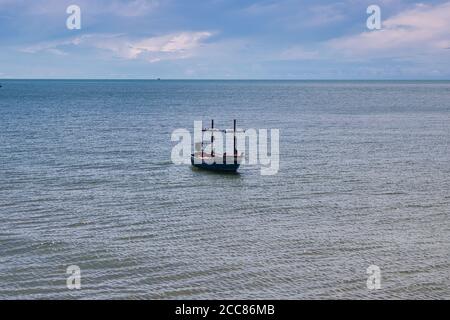 Questa foto unica mostra una tradizionale barca da pesca tailandese in legno che galleggia nell'Oceano Pacifico con mari calmi e cieli blu con nuvole bianche. Foto Stock