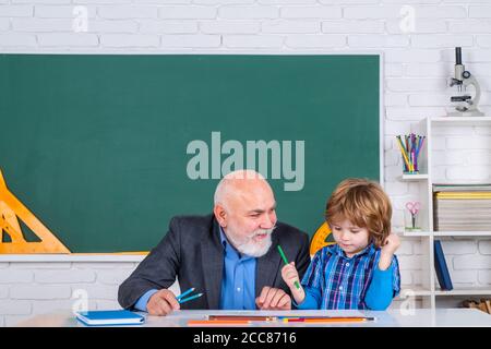 Happy Son e Grandfather seduti su una scrivania all'interno. Amico uomo bearded con vecchio insegnante maturo in classe. Foto Stock