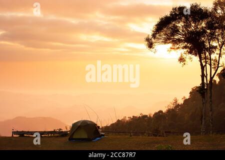 Campeggio tenda sulla cima della montagna all'alba, drammatica alba cielo su catena montuosa sullo sfondo. Motivazione, concetti di Avventura. Foto Stock