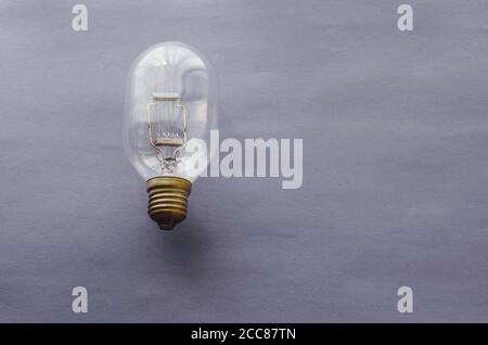 Lampada a incandescenza per illuminazione industriale su sfondo grigio-blu. Lampada in vetro con filamento di tungsteno antico. Spazio di copia. Messa a fuoco selettiva. Foto Stock