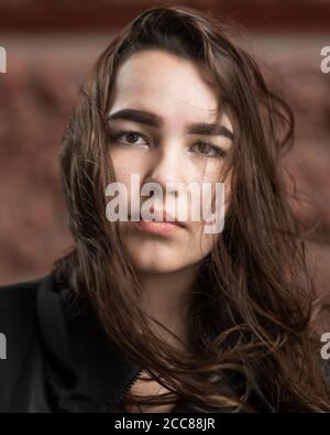 Giovane donna con i capelli sbucciati dal vento guarda la fotocamera Foto Stock