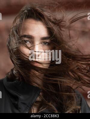 Giovane donna con i capelli sbucciati dal vento guarda la fotocamera Foto Stock