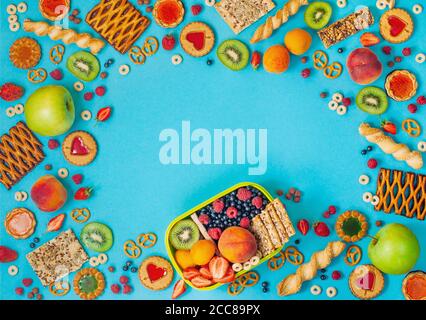 Cornice con pranzo al sacco e assortimento di frutta, frutti di bosco e grappoli su sfondo blu Foto Stock