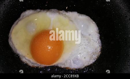 foto delle uova fritte di un uovo su un nero primo piano della padella Foto Stock