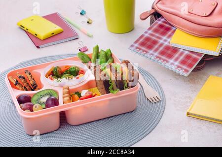 Pranzo al sacco con panini, insalata di verdure, frutta fresca e noci sul tavolo vicino zaino scuola Foto Stock