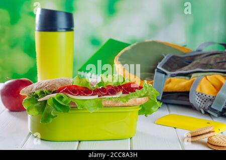 Pranzo al sacco con sandwich vicino thermos tazza, mela, biscotti, zaino e cellulare Foto Stock