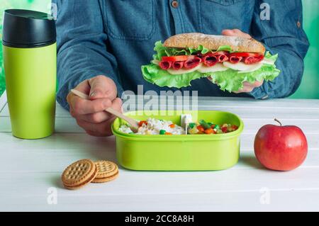 Mani di maschi che tengono panino e thermos tazza durante il mangiare il suo pranzo Foto Stock