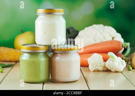 Tre vasetti con purea vegetale sullo sfondo di legno chiaro broccoli, cavolfiore, patate, carote Foto Stock