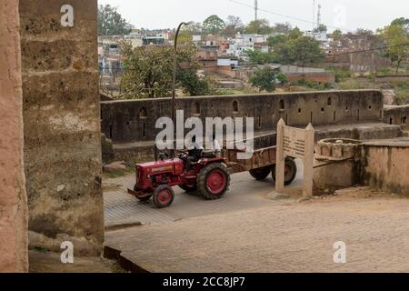 Orchha, Madhya Pradesh, India - Marzo 2019: Due uomini indiani cavalcano un trattore su una strada attraverso le antiche mura del forte storico nel villaggio di o Foto Stock