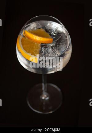 Cocktail con fette arancioni e cubetti di ghiaccio in un elegante bicchiere a gambo di Hugh su sfondo nero. Ripresa dall'alto con messa a fuoco selettiva . Foto Stock