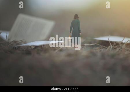 momento surreale di una donna con la lanterna che cammina confuso dentro la nebbia tra pagine e libri Foto Stock