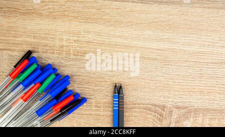 Pila di penne a sfera in plastica multicolore molto su tavolo di legno. Sfondo astratto di cancelleria. Vista dall'alto, disposizione piatta. Spazio di copia per il testo. forma 16x9 Foto Stock