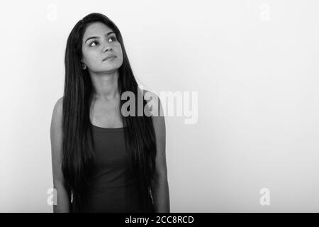 Studio shot della giovane donna indiana pensare guardando in alto e indossando sleeveless contro uno sfondo bianco Foto Stock