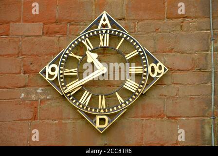 Orologio, datato 1909 d.C., con faccia rotonda montata su una cornice quadrata con angoli rivolti verso l'alto e verso il basso, chiesa di San Pietro, Martley, Worcestershire, Inghilterra Foto Stock