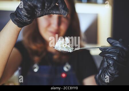 Barista che indossa guanti medici in lattice nero, tenere il cucchiaio con panna montata. Processo di preparazione del dessert in cafe.immagine sfocata, fuoco selettivo Foto Stock