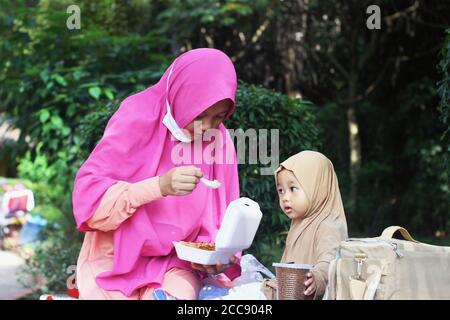 Una bella ragazza musulmana indonesiana carina di essere nutrita da sua madre nel parco Foto Stock