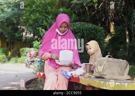 Una bella ragazza musulmana indonesiana carina di essere nutrita da sua madre nel parco Foto Stock