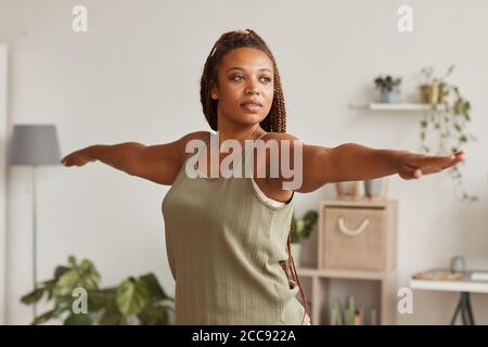 Giovane donna africana che allunga le mani che fa esercizi sportivi a casa Foto Stock