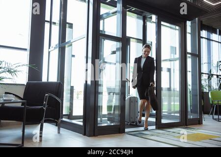 Saluto. Incontro di giovani partner d'affari dopo l'arrivo al punto finale del viaggio d'affari. Uomo e donna camminano contro lo sfondo di una parete di vetro di un edificio moderno. Concetto di business, finanza, annuncio. Foto Stock