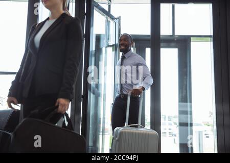 Saluto. Incontro di giovani partner d'affari dopo l'arrivo al punto finale del viaggio d'affari. Uomo e donna camminano contro lo sfondo di una parete di vetro di un edificio moderno. Concetto di business, finanza, annuncio. Foto Stock