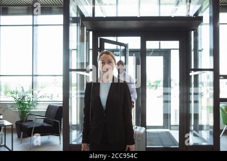 Saluto. Incontro di giovani partner d'affari dopo l'arrivo al punto finale del viaggio d'affari. Uomo e donna camminano contro lo sfondo di una parete di vetro di un edificio moderno. Concetto di business, finanza, annuncio. Foto Stock