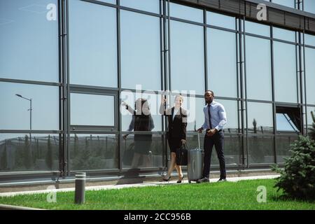 Presentazione. Incontro di giovani partner d'affari dopo l'arrivo al punto finale del viaggio d'affari. Uomo e donna camminano contro lo sfondo di una parete di vetro di un edificio moderno. Concetto di business, finanza, annuncio. Foto Stock