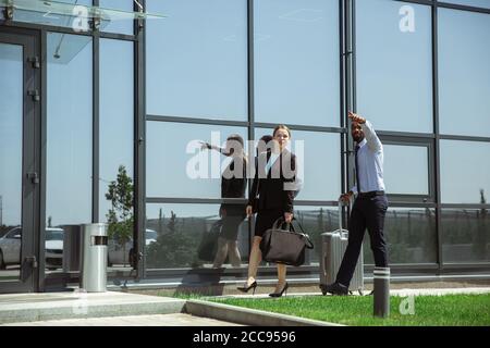 Presentazione. Incontro di giovani partner d'affari dopo l'arrivo al punto finale del viaggio d'affari. Uomo e donna camminano contro lo sfondo di una parete di vetro di un edificio moderno. Concetto di business, finanza, annuncio. Foto Stock