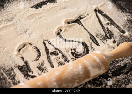 scritta sulla pasta scritta sulla farina vicino al mattarello su nero sfondo Foto Stock