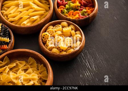 Fuoco selettivo di varie paste italiane crude in ciotole di legno su sfondo nero Foto Stock