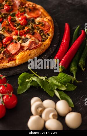 Focalizzazione selettiva della deliziosa pizza italiana con salame vicino alle verdure su sfondo nero Foto Stock