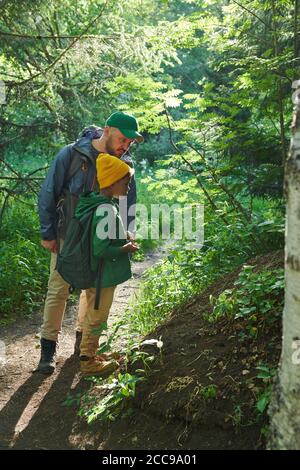 Padre e figlio esaminano alberi e cespugli durante il loro trekking nella foresta Foto Stock