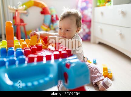 Bambina (16 mesi) seduta sul pavimento e giocando nella sua camera da letto con Colorati blocchi di plastica Mega Bloks® vicino al suo petto di legno bianco di cassetti