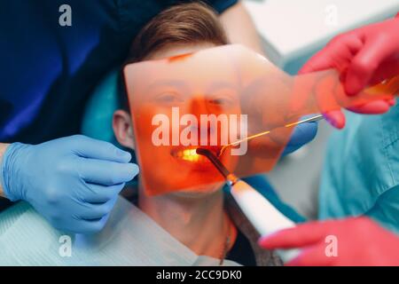 Odontoiatria. Dentista e paziente. Guarnizione indurente leggera. Lampada da denti UV e vetro protettivo arancione. Foto Stock