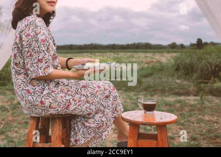 Donna asiatica che mangia cheesecake con una tazza di caffè all'aperto. Foto Stock