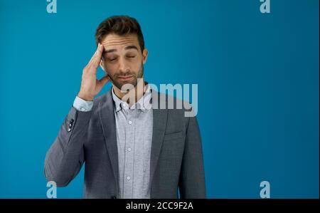 Giovane uomo d'affari che guarda stressato di fronte ad uno sfondo blu Foto Stock